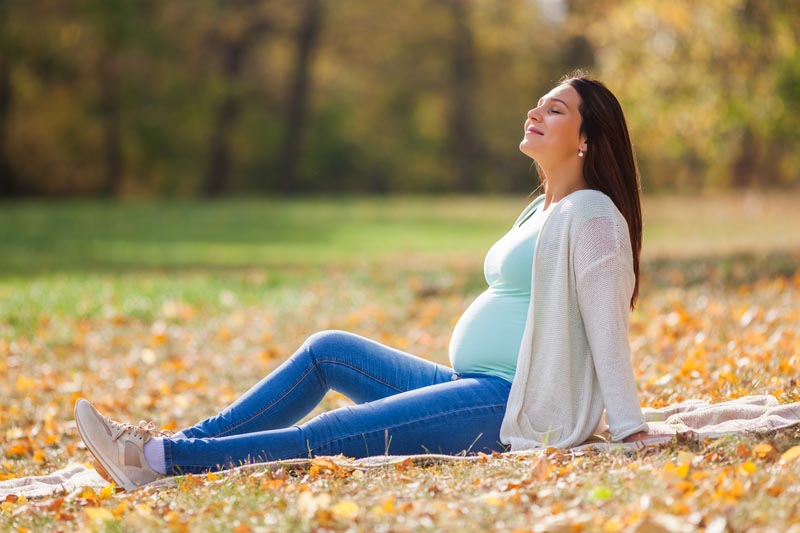 Glückliche schwangere Frau liegt im Park auf dem Boden
