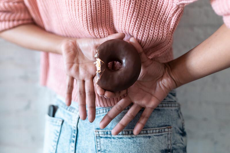 Junge Frau versteckt einen angebissenen Donut