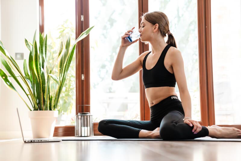 Junge Frau macht Yoga und trinkt nebenbei Wasser