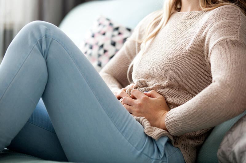 Junge Frau mit Menstruationsbeschwerden liegt auf dem Sofa
