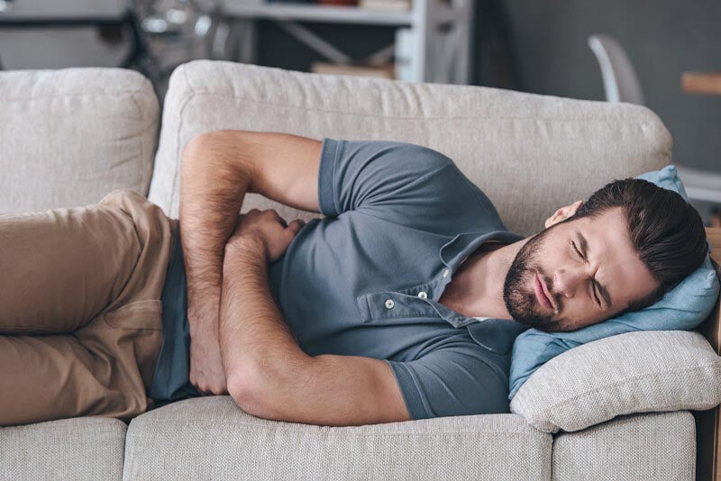 Mann mit einer Glutenunverträglichkeit liegt auf dem Sofa mit Bauchschmerzen